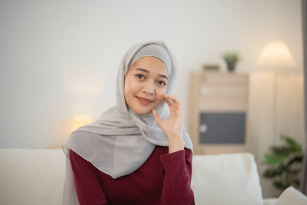 muzułmańska islamistka ubrana w hidżab lub szary szalik siedzi na kanapie. uśmiecha się i patrzy w kamerę - east asian ethnicity elegance lifestyles looking at camera zdjęcia i obrazy z banku zdjęć