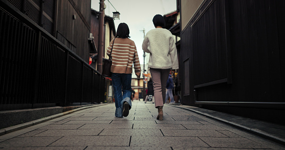 Women, walking and back by city street and travel for bonding in urban town in winter. Friends, wellness and commute together in neighborhood for social trip, vacation and outdoor in tokyo on journey