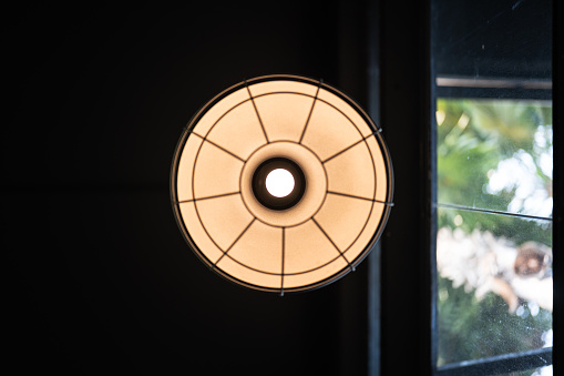 A classic style round ceiling lamp with glowing lightbulb in warm light shade, with dark area as background. Interior decoration and object photo, close-up.