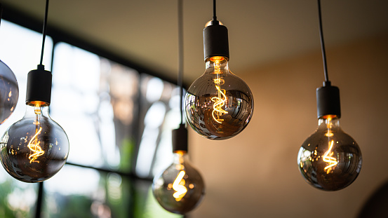 Classic lighting bulbs are glowing in orange warming shade, there are hanging from ceiling for Interior cozy style decoration. Close-up and selective focus.