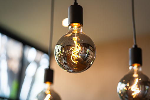 Classic lighting bulbs are glowing in orange warming shade, there are hanging from ceiling for Interior cozy style decoration. Close-up and selective focus.