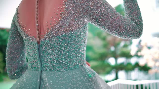 Elegant woman in a glittery green dress with a focus on the sleeve detail, blurred background.