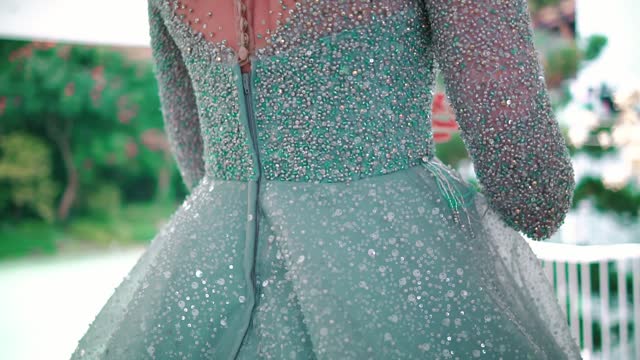 Elegant woman in a glittery dress outdoors, close-up on back detail with natural background.