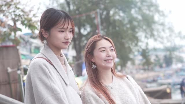 The image is of two Asian young women standing close to one another and smiling. They are both wearing casual clothes.