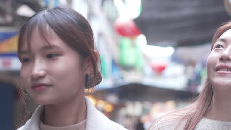 The image of two young Asian women walking down a busy street. They are both smiling and talking.