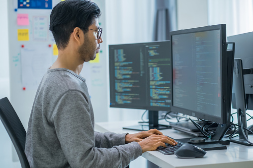 Asian prompt engineer developer coding app with software data sitting in front of computer monitor at office