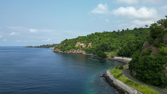 A car drives along the north coastal road between cliffs and the sea in Sao Tome and Principe, Africa