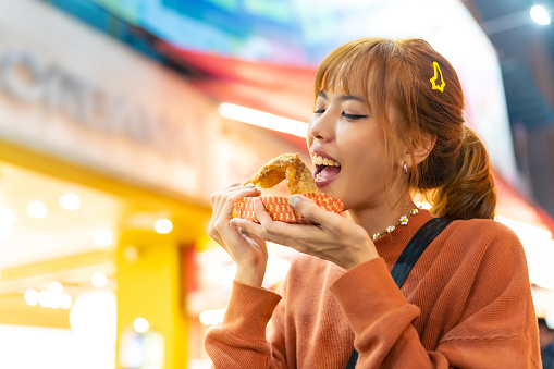 Young Asian woman tourist buying and eating street food Chinese sweet dessert snacks at night market near Ximen in Taipei, Taiwan. Attractive girl traveler enjoy and fun outdoor lifestyle travel and shopping in the city on summer holiday vacation.