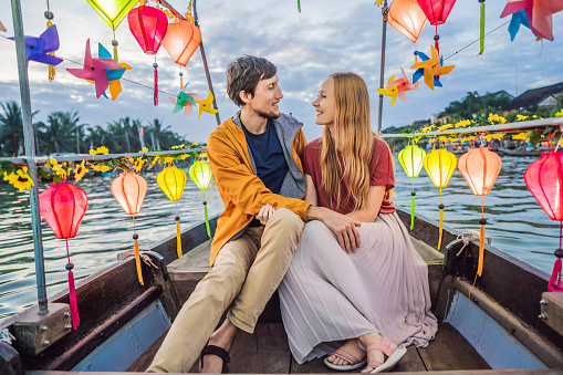 Happy couple of travelers ride a national boat on background of Hoi An ancient town, Vietnam. Vietnam opens to tourists again after quarantine Coronovirus COVID 19.