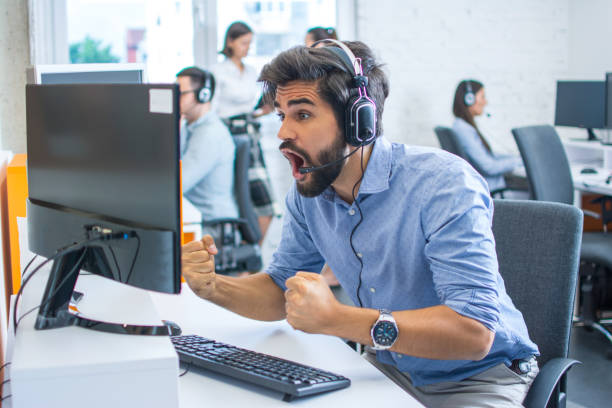 istock Euphoric handsome male operator agent with headset raising fists, screaming and staring at computer monitor in office. 2085598245