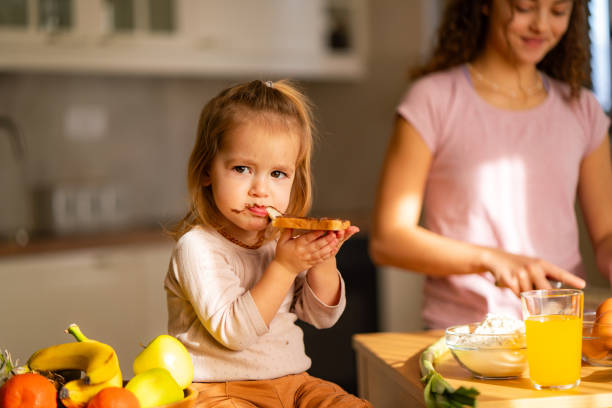 istock Cute little girl eating bread and chocolate spread while sitting in the kitchen 2085621827