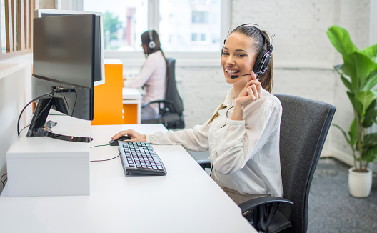 Portrait of happy smiling female customer support phone operator at workplace