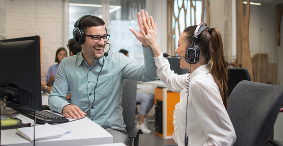 Cheerful customer support operators giving high-five to each other, celebrating a sale or success at work