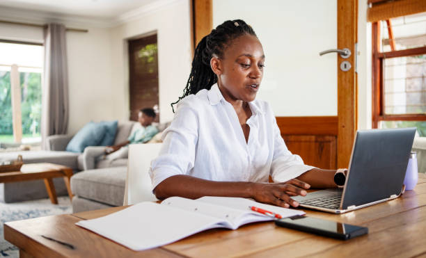 istock Mom using a laptop with her son playing a video game behind her 2085661415