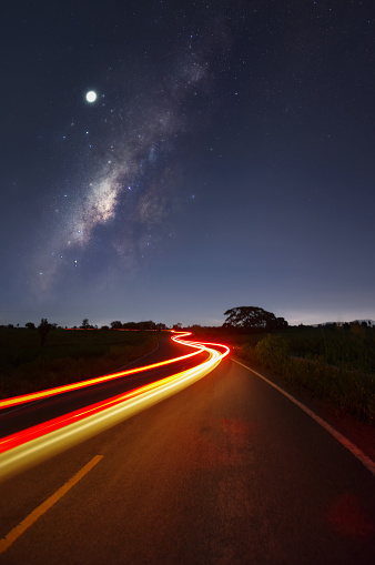 A vertical photograph of the Milky Way on a road with lights taken from the back of a car in Mae Moh District, Lampang Province, Thailand.