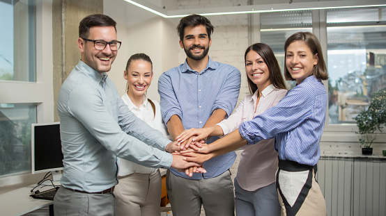 Group of business co-workers stacking hands together showing their team unity at office