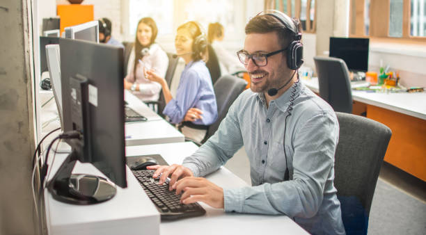 istock Smiling male call center worker accompanied by his team in row at modern office. 2085672233