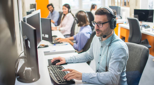istock Male customer service representative with headset working in call center office with colleagues in row. 2085674341