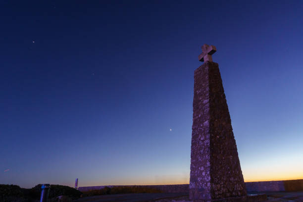 cross on a stone pillar at cabo da roca under the night sky with planets venus, saturn and jupiter during evening twilight, sintra, lisbon, portugal - sintra sunset cross outdoors ストックフォトと画像