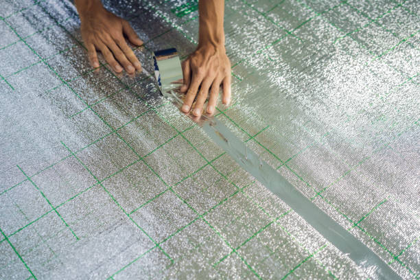 Master installs the overlapping thermal insulation in the room. Floor heating installation. Male hand holds reinforced tape. Repair in the apartment, floor insulation