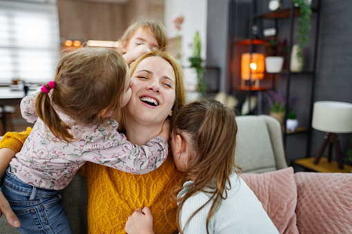 Affectionate mother playing with her three little daughters at home
