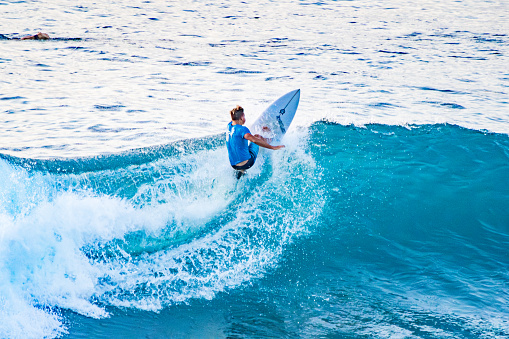 Bali, Uluwatu - A surfer, balanced on a surfboard, rides a turquoise wave. Blue ocean in the background.