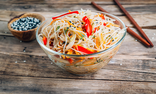 Cold Funchoza salad. Glass noodles salad with fresh vegetables: carrot, bell pepper, cucumber, with sesame seeds. Asian food. Wooden background. Selective focus