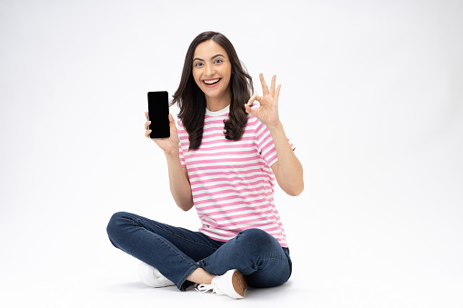 Full size photo of pretty young girl sit floor showing device screen wear trendy outfit isolated on white background