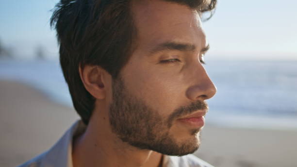 istock Sexy bearded man looking camera with daring smile posing on ocean coast close up 2085749533