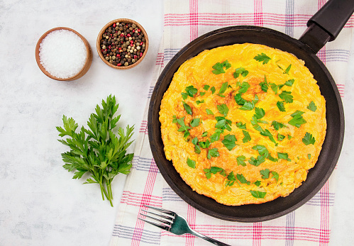 Delicious homemade egg omelette with parsley in a pan on a gray background top view