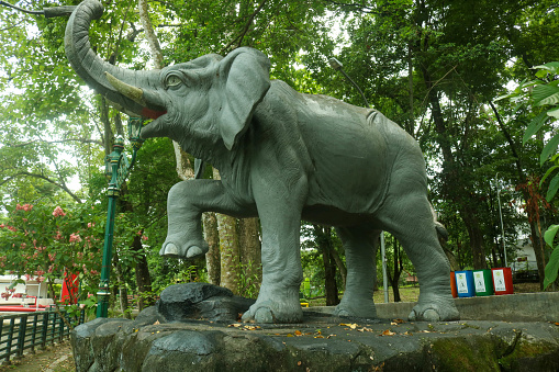 Indonesia - March 3 2024: Gray elephant statue at Gadjah Mada University lake surrounded by lush trees. Lake park in the city with fountain elephant statue
