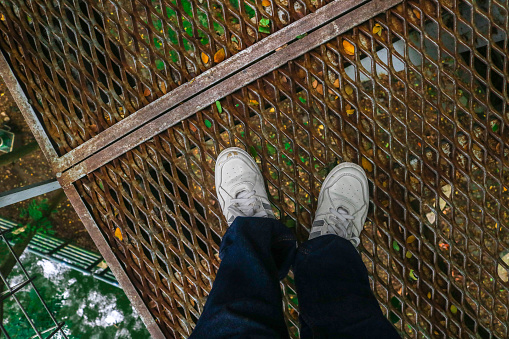 Feet in jeans and white sneakers standing on a rusty iron bridge surrounded by trees