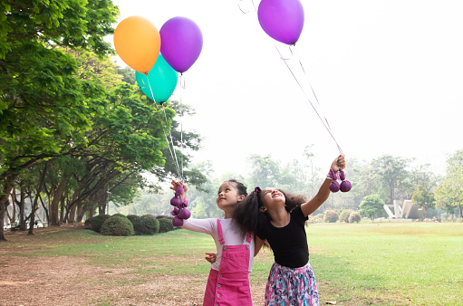 Portrait of two children standing together looking camera smiling, joyfully waving colorful balloons, Happy kids friends enjoy carefree childhood playtime, healthy primary school outdoor activities