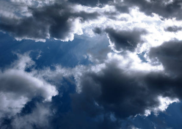 Bright light of the sun on a dark blue sky among the clouds. Dramatic view of the sun.