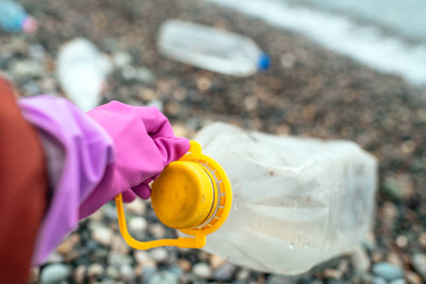 Woman's hand picking up plastic garbage on a sea shore. Plastic pollution and global ocean ecological and environment problems concept.