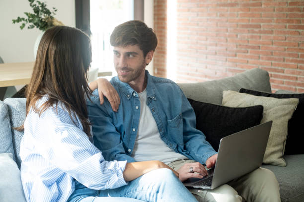 istock Young married couple sitting on sofa in the living room at home using tablet PC for internet and social media. Happy family resting on couch enjoying weekend watching video or talking on video call. 2085805496