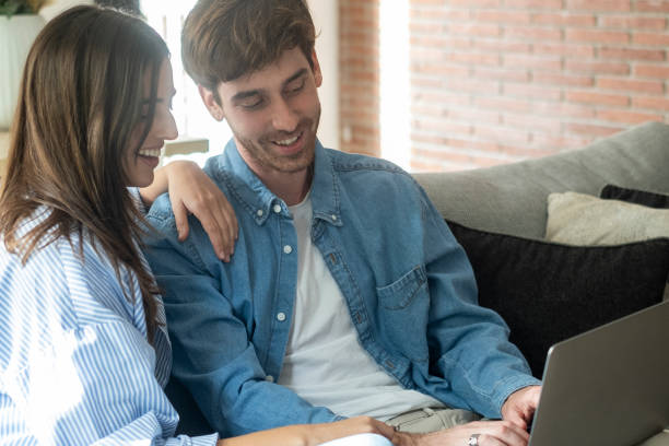 istock Young married couple sitting on sofa in the living room at home using tablet PC for internet and social media. Happy family resting on couch enjoying weekend watching video or talking on video call. 2085806018