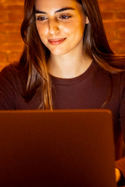 istock Beautiful Authentic Young Woman Sitting at a Table in Cozy Kitchen and Using Laptop Computer at Home at Night. Female Smiling and Chatting on the Internet and Social Media, Doing Online Research. 2085821757