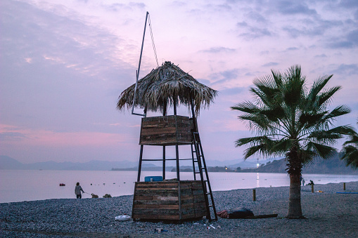 A beautiful beach on a sunset with pink sky. Lifeguard booth near to palm trees. Fethiye, Turkey.