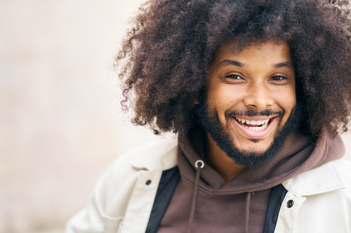A man with a beard and dreadlocks is smiling and wearing a brown hoodie