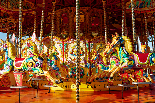 A happy mother and son are riding on a carousel together, smiling and having fun at an amusement park.  The boy holds two thumbs up.