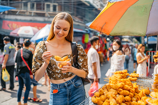 Beautiful young woman buying patonggo (Thai-style Chinese fried dough) at the street market in Chinatown in Bangkok in Thailand.