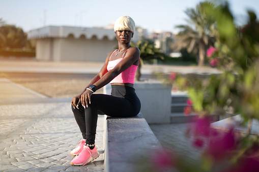 Young fitness black woman with blond hair wearing sports clothes sitting on concrete wall outdoors