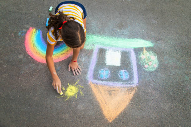 A child draws a house and a rainbow on the asphalt with chalk. Selective focus.