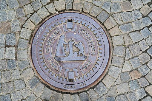 Stavanger, Norway - 05 29 2022: lid of a man hole in the historic city center of Stavanger with typical norwegian architecture.