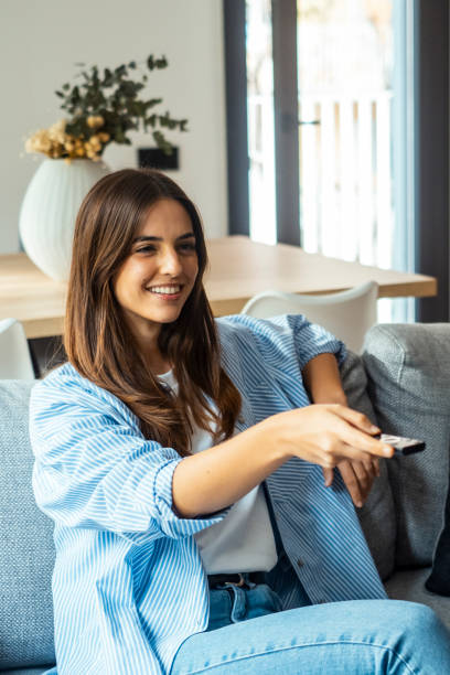 istock young woman sitting on her home sofa, holding the TV remote while enjoying a program. she is enjoying her leisure time at home. One female people using control tv watching movie alone on the couch 2085881560