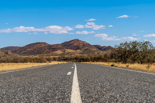 Outback road near Alice Springs with the East Macdonnell Range on the horizon. Northern Territory, Australia.