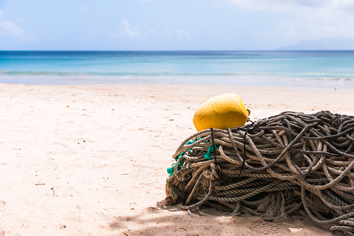 Old fishing nets with yellow float lay on white sand of Beau Vallon Beach under cloudy sky, Seychelles