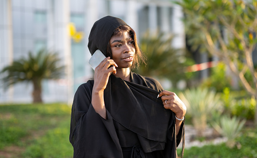 Portrait of young African muslim woman wearing abaya talking on phone outdoors