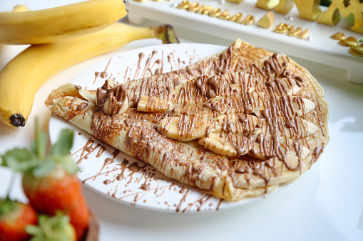 A white plate holds a delectable banana split topped with a generous drizzle of chocolate sauce.